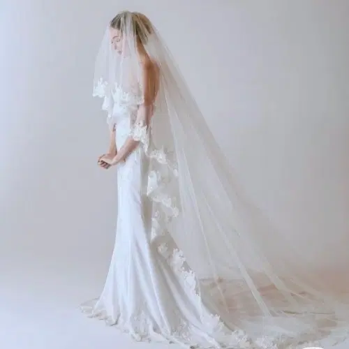 Mariée de profil en robe blanche, sous un long voile bordé de dentelle